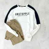 Buzo blanco de algodón con mangas raglán negras y estampa frontal con la palabra "UNSTOPPLE" y la frase "DUXON COLLECTION" en negro.