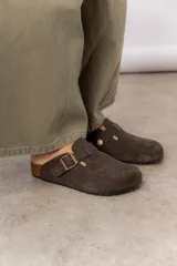 Zuecos de cuero color marrón oscuro, con suela de corcho y hebilla regulable dorada.