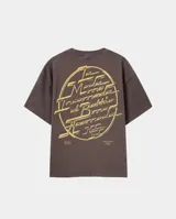 Remera de corte oversize color marrón oscuro, con estampa gráfica circular en color crema en la espalda que presenta tipografía estilizada y detalles de texto en la parte inferior.