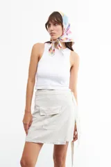 Minifalda color beige de lino y viscosa, con corte cruzado, lazo lateral y bolsillo tipo cargo.