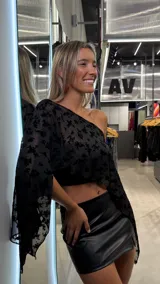 Top tipo capa de un solo hombro, confeccionado en tul negro con diseño floral aterciopelado. Presenta un corte asimétrico y holgado con mangas amplias.