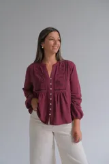Blusa de manga larga color bordó con cuello mao y cierre frontal de botones. Presenta detalles de bordados florales y calados en el frente, con un corte holgado y puños elásticos.