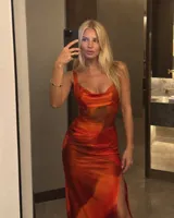 Vestido largo de microtul estampado en tonos naranjas y rojos, con escote drapeado y tirantes anchos. Presenta un diseño ajustado que realza la silueta con transparencias en la zona de la cintura.