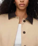Chaqueta boxy acolchada de algodón en color beige, con cuello italiano de piel ovina en contraste, manga larga con hombro caído y bajo abullonado. Cuenta con cierre de botones y bolsillos de vivo inclinados en el delantero.