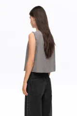 Top corto sin mangas de corte recto, con estampa de cuadros vichy en tonos negro y blanco. Presenta escote redondo, cierre frontal con múltiples lazos para atar y detalles desflecados en sisa y cuello.