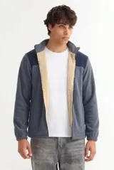 Campera de polar color gris con recortes en los hombros de tono azul marino, cuello alto y forro interno de corderito en color beige. Cuenta con cierre frontal y bolsillos laterales.