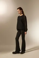 Blusa negra de poliéster con diseño texturizado de ondas, cuello redondo a la base y mangas largas transparentes con puños elásticos.