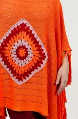 Poncho rojo de tejido artesanal con aplique central de crochet en forma de mandala con tonos amarillos, blancos y rojos. Presenta terminación con flecos en los laterales y diseño holgado.