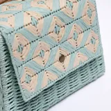 Bandolera celeste de paja trenzada con diseño geométrico en beige y correa de cuero sintético marrón.