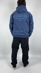 Canguro azul con capucha, corte oversize y estampado en el frente con la leyenda "Duxon Co." en letras mayúsculas, seguido de texto en japonés y la palabra "Tokyo".