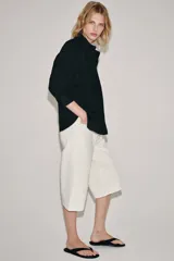 Camisa de cuello redondo y manga corta abullonada, color negro, de corte recto con aberturas laterales y cierre frontal con botones. Perteneciente a la colección ZARA Woman Collection.