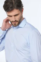 Camisa celeste entallada de manga larga con cuello clásico y cierre frontal con botones. Pantalón de vestir azul marino con cinturón de cuero marrón.