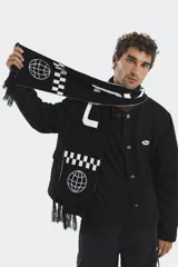 Bufanda tejida de punto con diseño gráfico en blanco y negro, que incluye motivos de globos terráqueos y patrones de damero. Presenta flecos en los extremos y un estilo urbano.