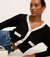 Cardigan de punto blanco con escote en V, botones metalizados, bolsillos falsos, cuello y vista contrastantes en negro, y bajo acanalado.