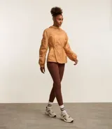 Campera deportiva femenina tipo parka, color ocre, confeccionada en poliamida y poliéster. Tiene cuello con capucha, mangas largas con puños elásticos, cierre frontal con cremallera y cordón ajustable en la cintura.