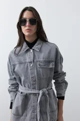 Sobrecamisa de jean color negro con silueta relajada, cuello camisero, cierre frontal con botones metálicos, bolsillos frontales y cinturón ajustable en la cintura.