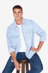 Camisa de jean celeste de manga larga, con cuello clásico, cierre frontal con botones a presión, dos bolsillos con solapa abotonada en el pecho, corte en hombros y detalle en la espalda.