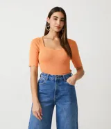 Blusa de punto acanalado color naranja, con escote cuadrado y mangas cortas con volados en los puños.