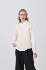 Chaleco de punto color natural, con escote en V, cierre frontal con botones y dos bolsillos delanteros aplicados.