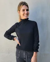 Polera negra de tejido acanalado con cuello alto y puños con detalle de punto smock y volados.