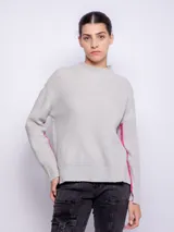 Suéter gris de punto con cuello alto, mangas largas y anchas, detalle de línea vertical rosa contrastante en las mangas y aberturas laterales.