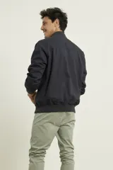 Campera tipo bomber color verde militar, confeccionada en 100% algodón. Cuenta con puños tejidos al tono, cuello y cintura elásticos, y cierre frontal metálico.