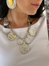 Collar plateado con cadena de eslabones y dijes colgantes de diferentes formas y tamaños, algunos con detalles dorados.