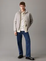 Campera Calvin Klein color gris claro, confeccionada en nailon 100% reciclado. Tiene cuello alto de canalé, puños y bajo elásticos, cierre de cremallera, bolsillos en la cintura, forro ligeramente acolchado y logo de la marca en el pecho y la manga.