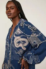 Blusa oversize azul con estampado integral en tonos claros, cuello en V con cordones ajustables, mangas largas abullonadas y puños elásticos.