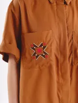 Camisa de manga corta color amarillo claro, con calce oversized, hombros caídos y cierre frontal con botones. Cuenta con bolsillos delanteros con bordados geométricos y mangas con dobladillo.
