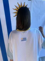 Remera de corte oversize confeccionada en tejido de punto acanalado color celeste, con mangas cortas en color amarillo y detalle de parche bordado con la bandera de Uruguay en la parte superior de la espalda.