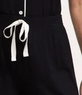 Conjunto de pijama corto negro con ribetes blancos, compuesto por una camisa de manga corta con cuello, bolsillo en el pecho y cierre abotonado, y un short con cintura elástica.