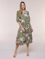 Vestido midi de silueta holgada en color blanco con estampado de hojas verdes. Presenta escote en V con cuello mao y botones frontales en la pechera, mangas tres cuartos abullonadas con puños elásticos y falda de corte evasé con niveles fruncidos.