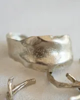 Brazalete rígido plateado con textura irregular.