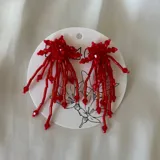 Caravanas colgantes de diseño artesanal, compuestas por múltiples hilos de cuentas de cristal en color rojo, con una estructura superior en forma de estrella.