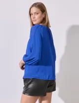 Blusa de gasa color azul, con cuello redondo y aberturas frontales en V. Presenta mangas raglán con apliques de puntilla a lo largo y puños fruncidos.