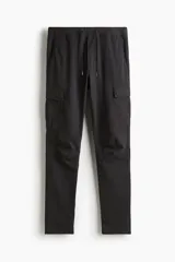 Pantalón cargo negro de corte slim fit, con cintura elástica ajustable con cordón, bolsillos laterales, bolsillos cargo con solapa y botones a presión ocultos, y pinzas en las rodillas.