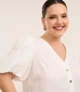 Blusa blanca de crepé con escote en V, abotonada en el frente y mangas cortas abullonadas.