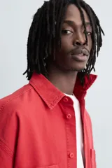 Camisa de algodón con estructura canvas, color rojo lavado, de corte relajado (relaxed fit) y manga corta. Posee cuello solapa, dos bolsillos de plastrón en el pecho y cierre frontal de botonadura. Presenta bordado y estampado de texto a contraste en el delantero.