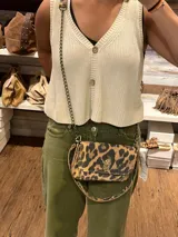 Minibag tipo acordeón con estampado animal print de leopardo. Cuenta con cierre frontal metálico, correa de cadena dorada y una correa de mano adicional. Su diseño estructurado permite organizar los objetos esenciales.