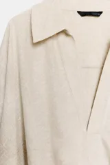 Camisa verde militar confeccionada en mezcla de lino, con cuello solapa, escote en pico, manga larga y diseño asimétrico con pliegues en la parte delantera.