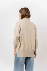 Sweater de tejido de punto color beige, con cuello alto, hombros caídos, mangas largas con puños acanalados y tajos laterales en el ruedo.
