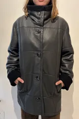 Campera de cuero color tostado con diseño de paneles, cuello alto y puños con forro de corderito sintético. Presenta cierre frontal con botones grandes y bolsillos laterales.