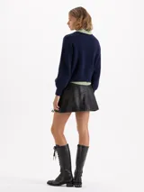 Mini falda de cuero ovino negro con efecto brush off, decorada con múltiples apliques de moños de cuero fijados con remaches metálicos. Posee bolsillos ojal en la parte trasera y forrería de acetato.