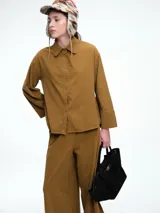 Camisa oversize de lyocell color tostado, con cuello clásico, cierre frontal de botones y mangas largas con puños anchos. Presenta un diseño de corte relajado con caída fluida.