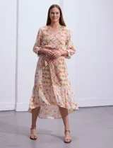 Vestido midi estampado con flores y mandalas en tonos naranja, rojo y celeste, con escote en V, mangas 3/4 con puños fruncidos, cintura elastizada con lazo y ruedo irregular.