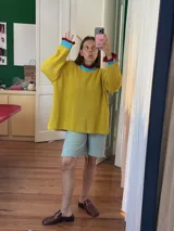 Buzo de punto oversize color rojo, con cuello alto y puños con terminaciones en volados. Presenta detalles en contraste color amarillo en el cuello y los puños, con un tejido de acabado ligeramente brillante.