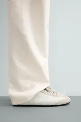 Zapatillas de cuero color blanco roto, de diseño minimalista con cordones, suela fina de goma marrón y detalles de gamuza en la puntera y los ojales.