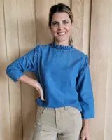 Blusa blanca de manga larga con cuello alto y volados en cuello y hombros.