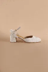 Zapato de tacón bajo y cuadrado en color beige, con punta cerrada redondeada y tira fina con hebilla ajustable al tobillo.